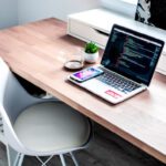 Coding - smartphone on laptop computer on top of brown wooden desk